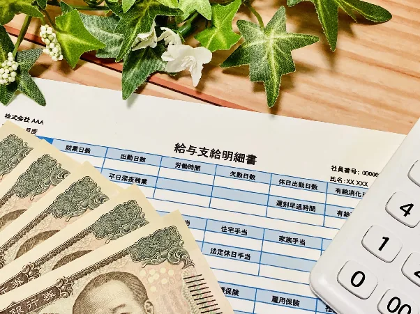 給与支給明細書と紙幣、電卓が並んだ机の上