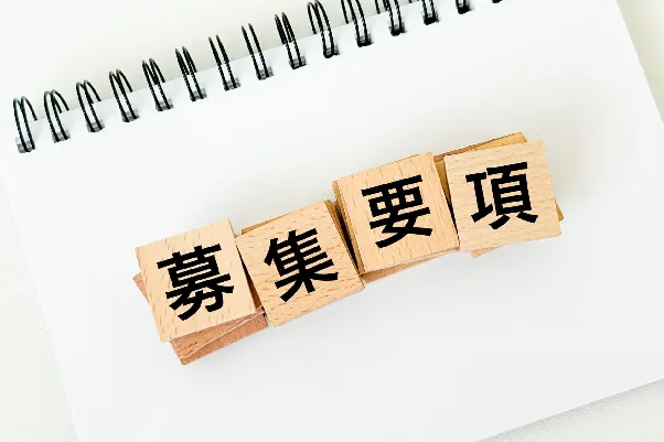 ノートの上に置かれた「募集要項」と書かれた木製ブロック